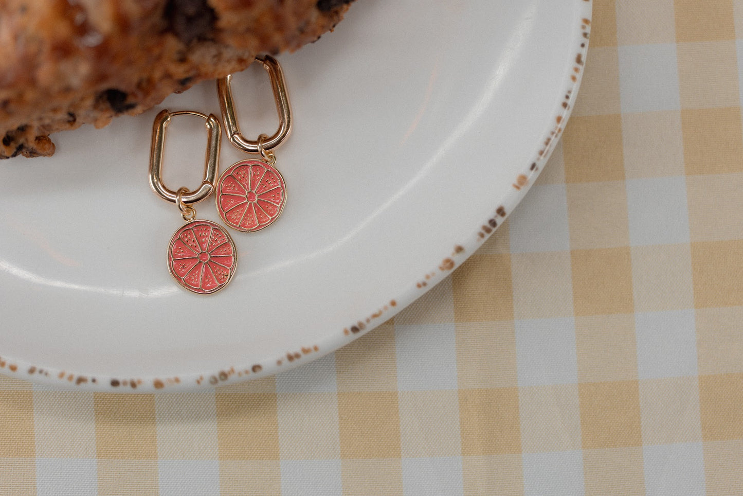 Pair of earrings with orange designs on a white plate with a checkered tablecloth.