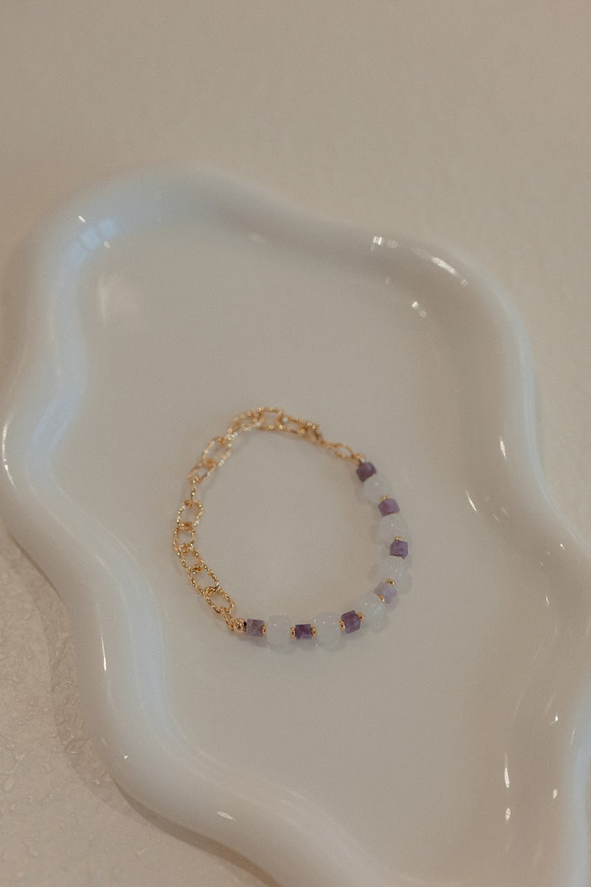 Gold bracelet with purple beads on a white dish