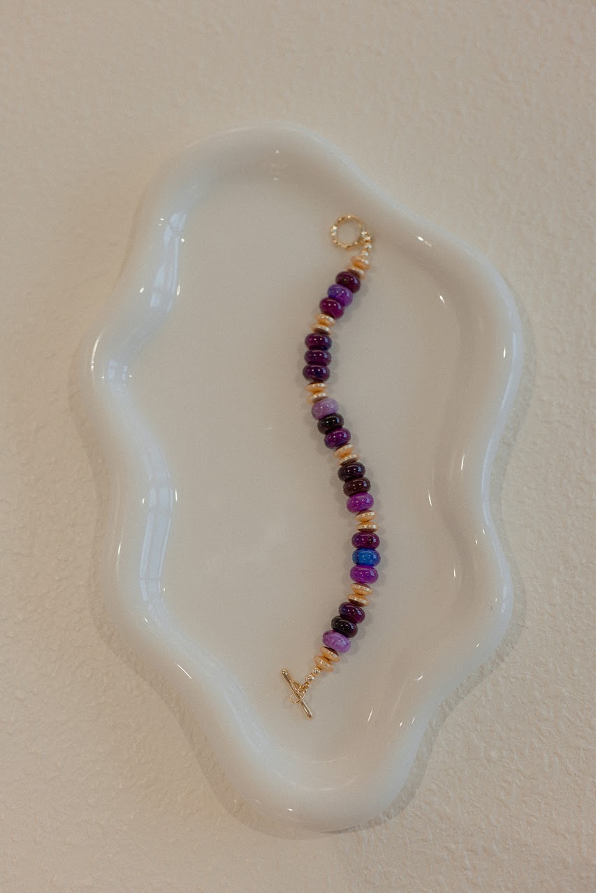 Beaded bracelet with purple and gold beads on a white dish
