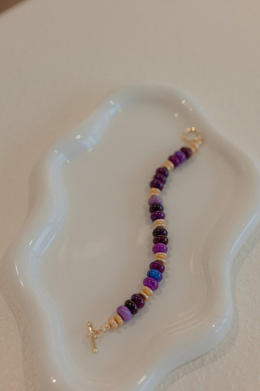 Beaded bracelet with purple and gold elements on a white dish