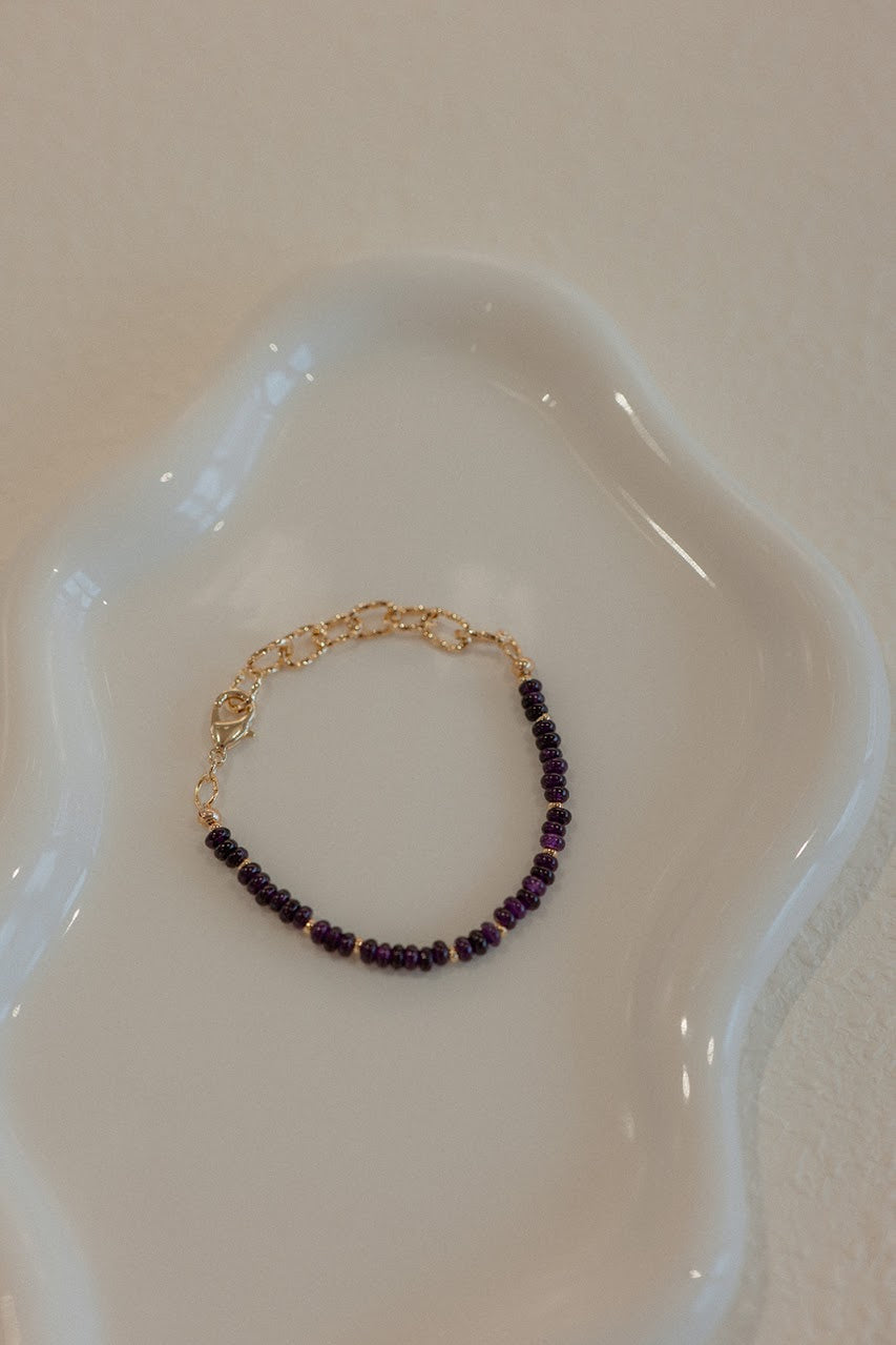 Gold bracelet with purple beads on a white dish