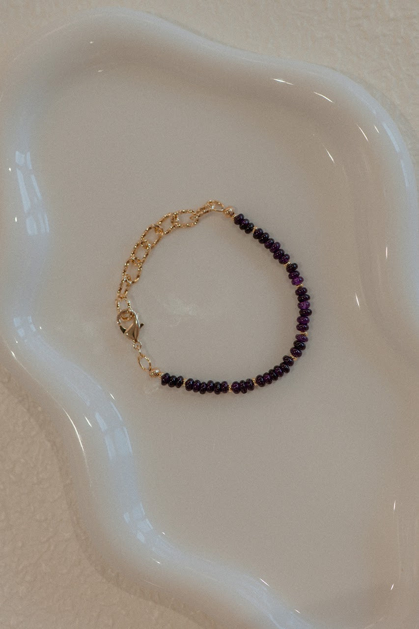 Bracelet with purple beads and gold accents on a white dish