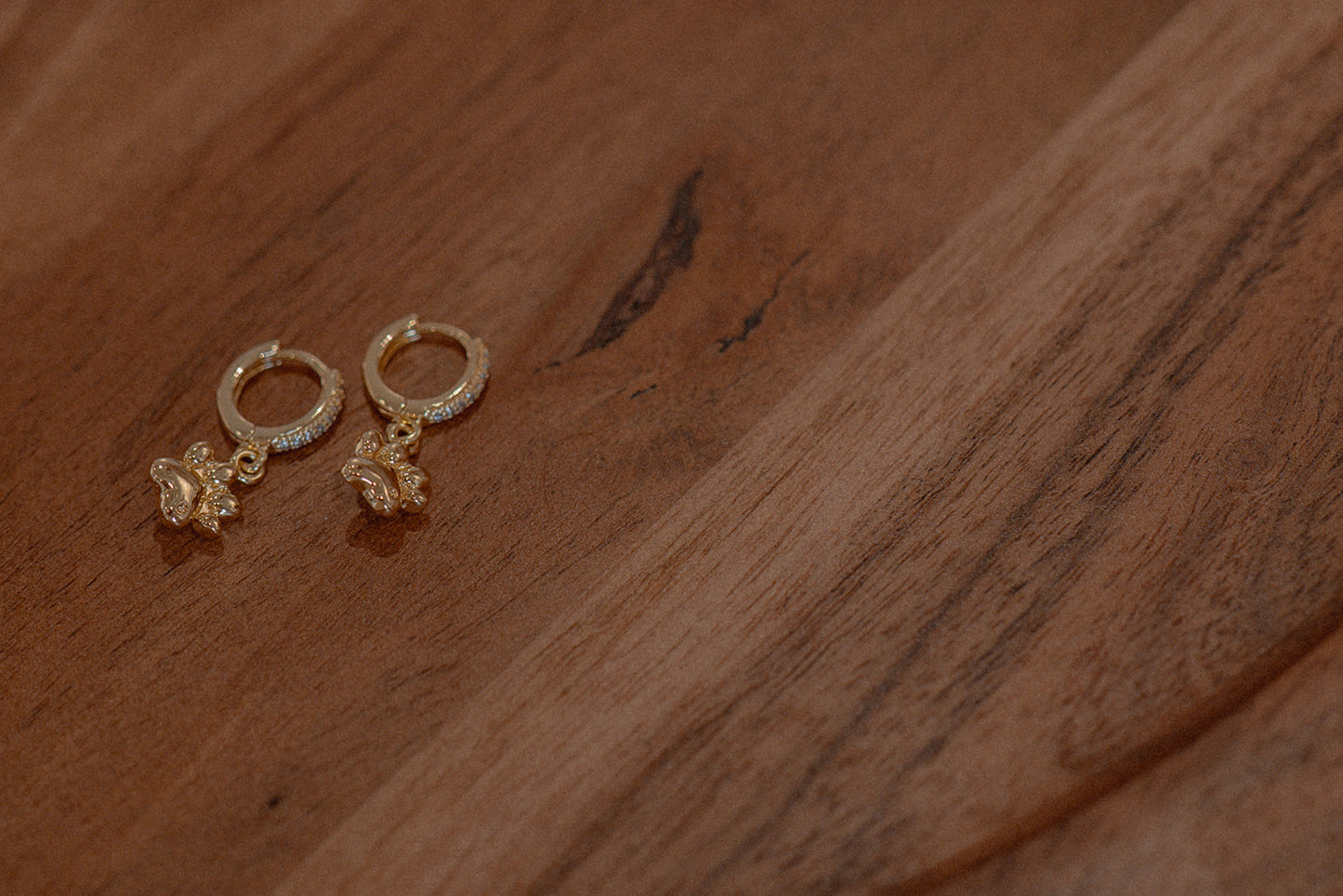 Gold earrings with floral designs on a wooden surface