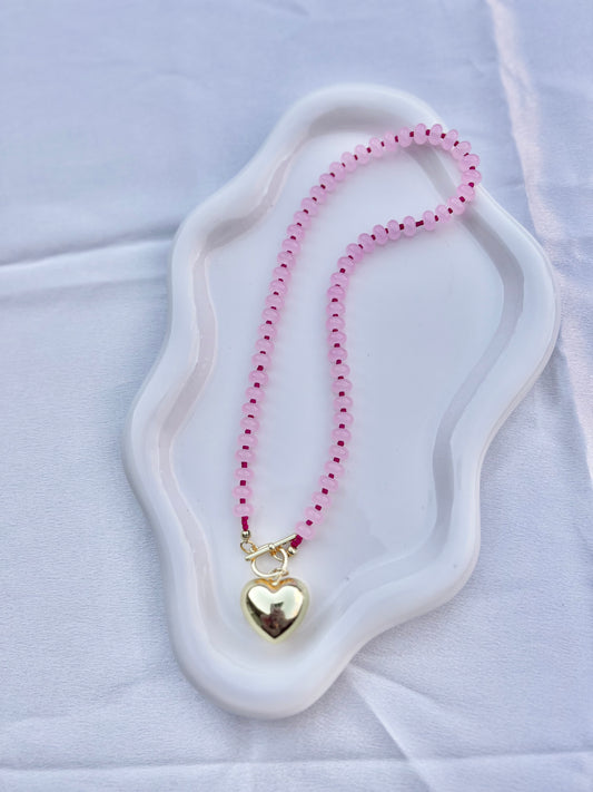 Necklace with pink beads and a gold heart pendant on a white surface