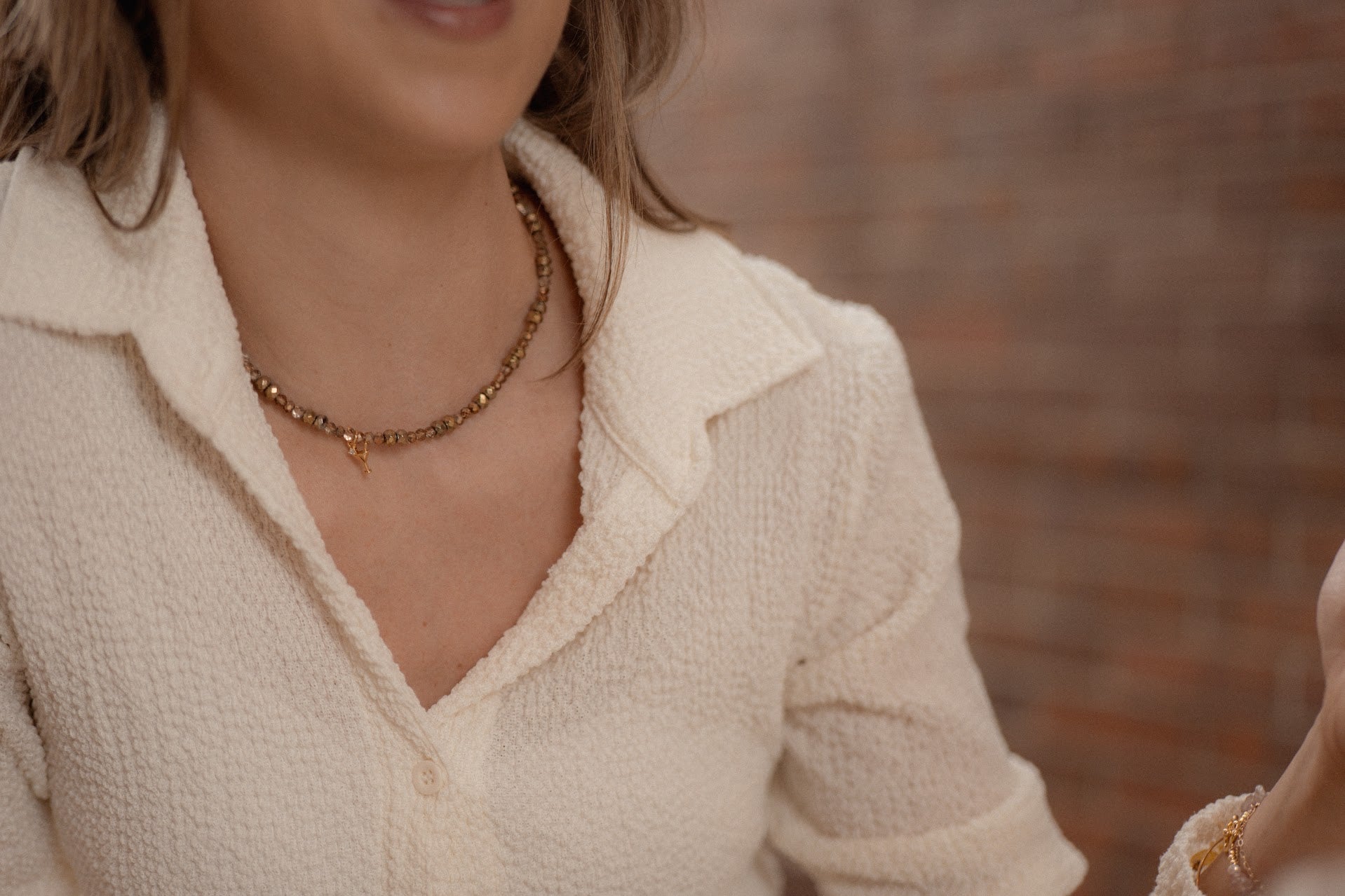 Close-up of a person wearing a beige textured top with a blurred brick wall background