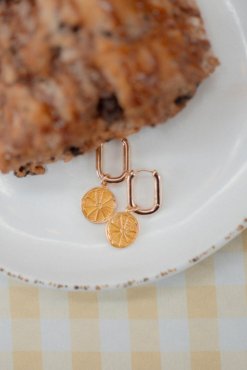 Gold earrings on a white plate with a piece of cake on a checkered tablecloth