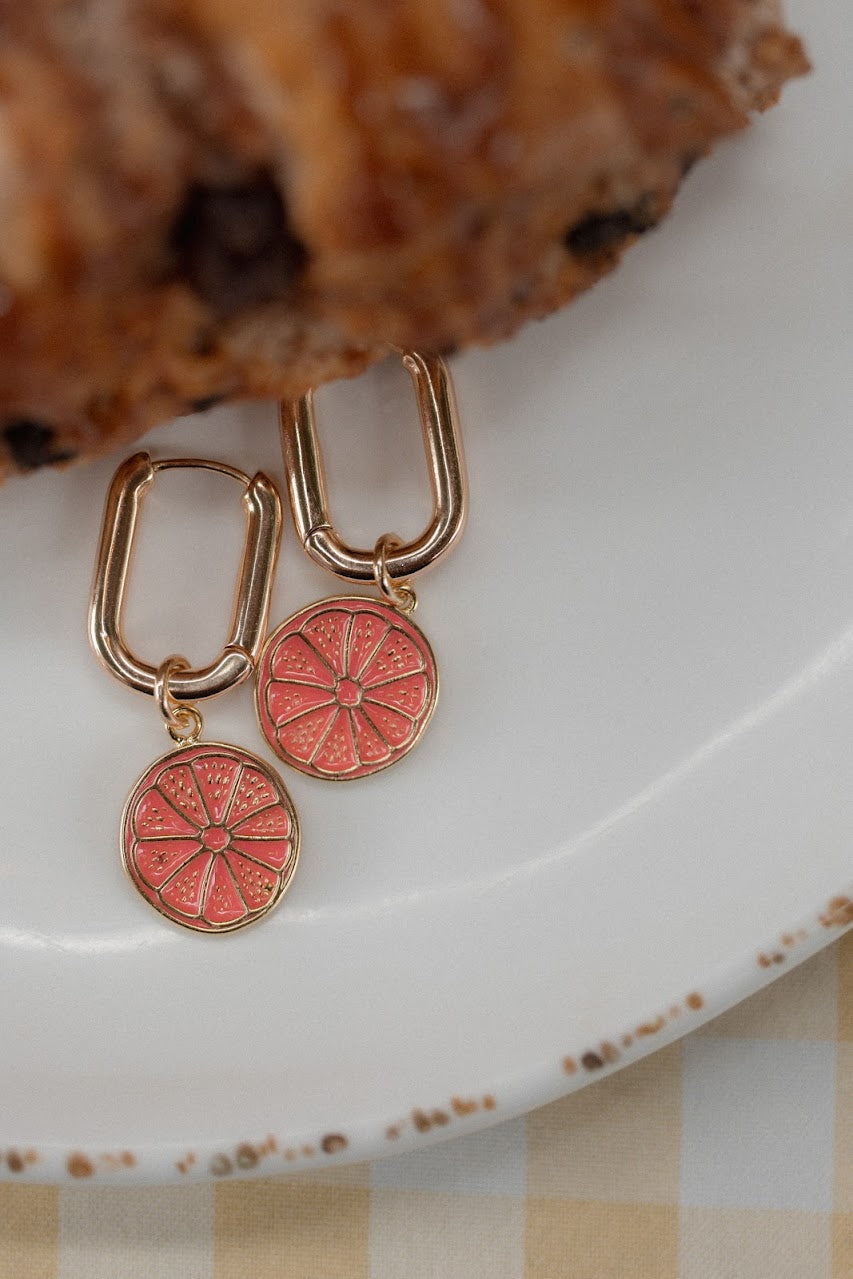 Pair of gold earrings with pink circular charms on a white plate.