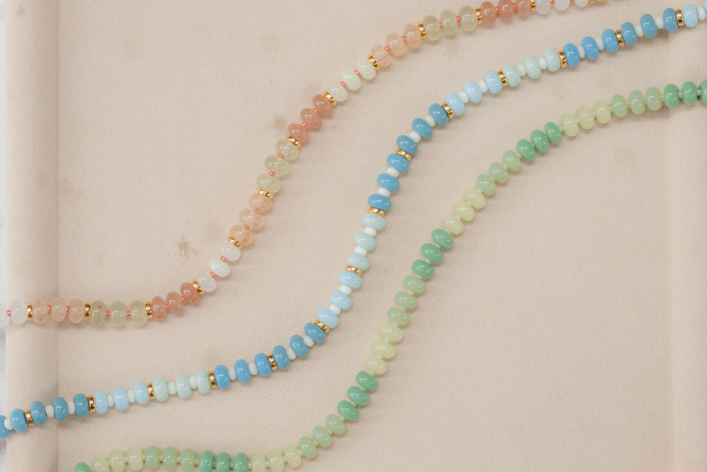 Three beaded necklaces in pastel colors on a beige background