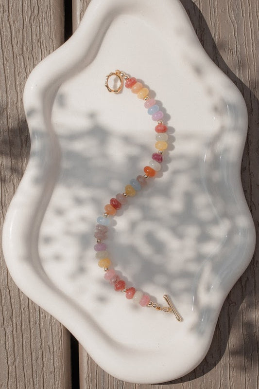 Colorful beaded bracelet on a white ceramic dish with wooden background