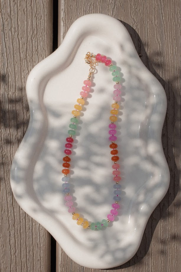 Colorful beaded necklace on a white ceramic dish against a wooden background