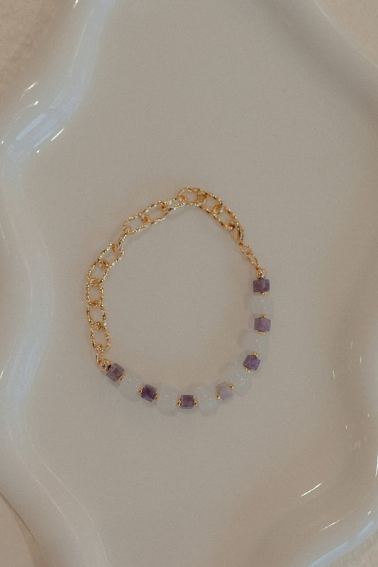 Gold bracelet with purple beads on a white dish