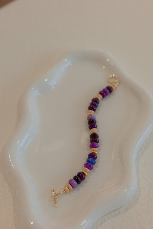 Beaded bracelet with purple and gold elements on a white dish