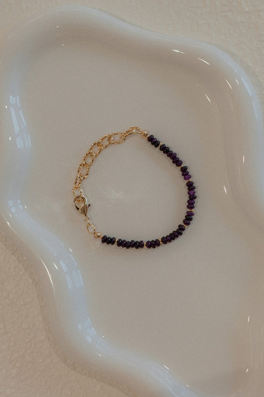 Bracelet with purple beads and gold accents on a white dish