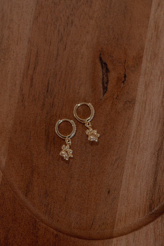 Gold hoop earrings with floral charms on a wooden surface